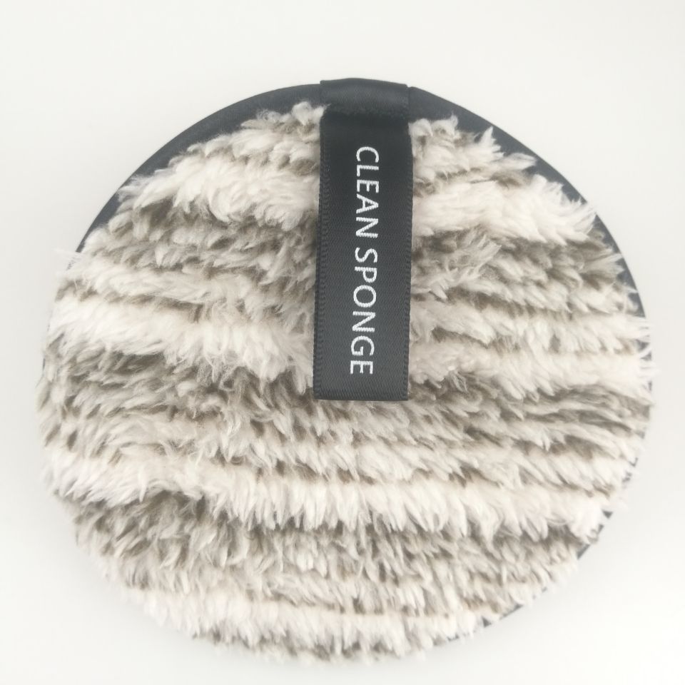Round, fuzzy, beige and brown makeup remover pad with a black "CLEAN SPONGE" label on a white background.