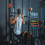 Man using a black metal power cage with orange accents and a bench to perform lat pulldowns in a gym.