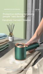 Portable green and gold handheld garment steamer steaming a beige fabric on a table.