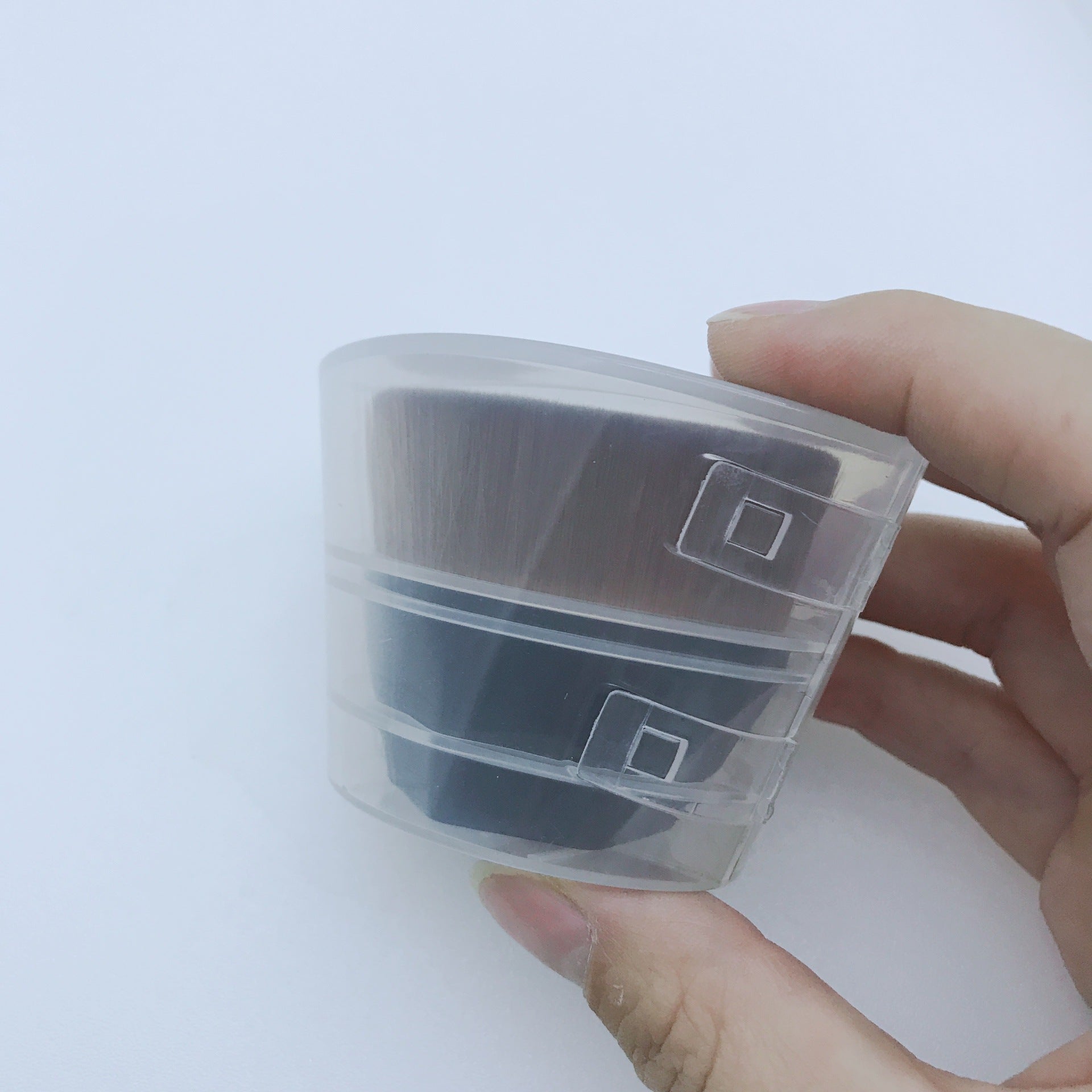 Hand holding a flat, dense makeup foundation brush inside a transparent plastic protective cap.