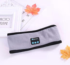 Grey fleece Bluetooth yoga headband with integrated control panel, placed on a white surface with decorative leaves.