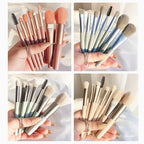 Four sets of 8 portable makeup brushes with metallic handles in pink, blue, sage, and beige, held in a hand.