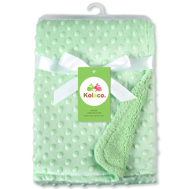 Mint green baby blanket with raised dots, wrapped in white ribbon with a Kolaco brand tag. Soft textured fabric.
