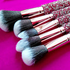 Makeup brushes with rose gold ferrules and pink diamond-inlaid handles, featuring black and white synthetic bristles.