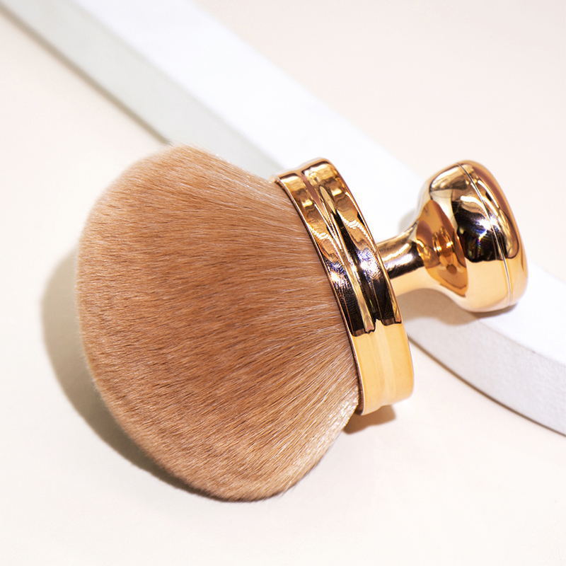 Oversized makeup brush with soft, dense tan bristles and a shiny, gold-finished metallic handle.
