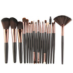 Set of makeup brushes with black handles, rose-gold ferrules, and dark brown bristles, including a fan brush.