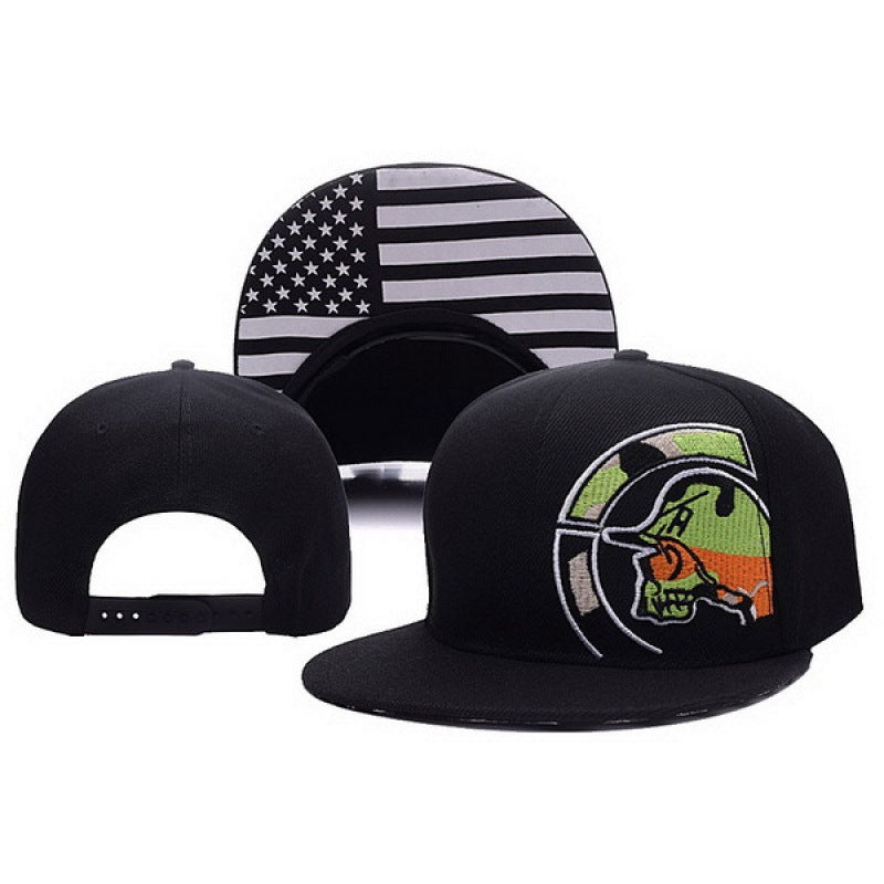 Black snapback hat with a green and orange skull graphic on the front and a US flag print under the brim.