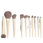 Set of nine makeup brushes with pale wooden handles and soft brown synthetic bristles against a white background.