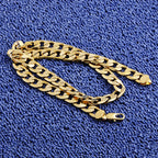 Gold-tone hip hop style curb chain necklace resting on a textured blue fabric surface.