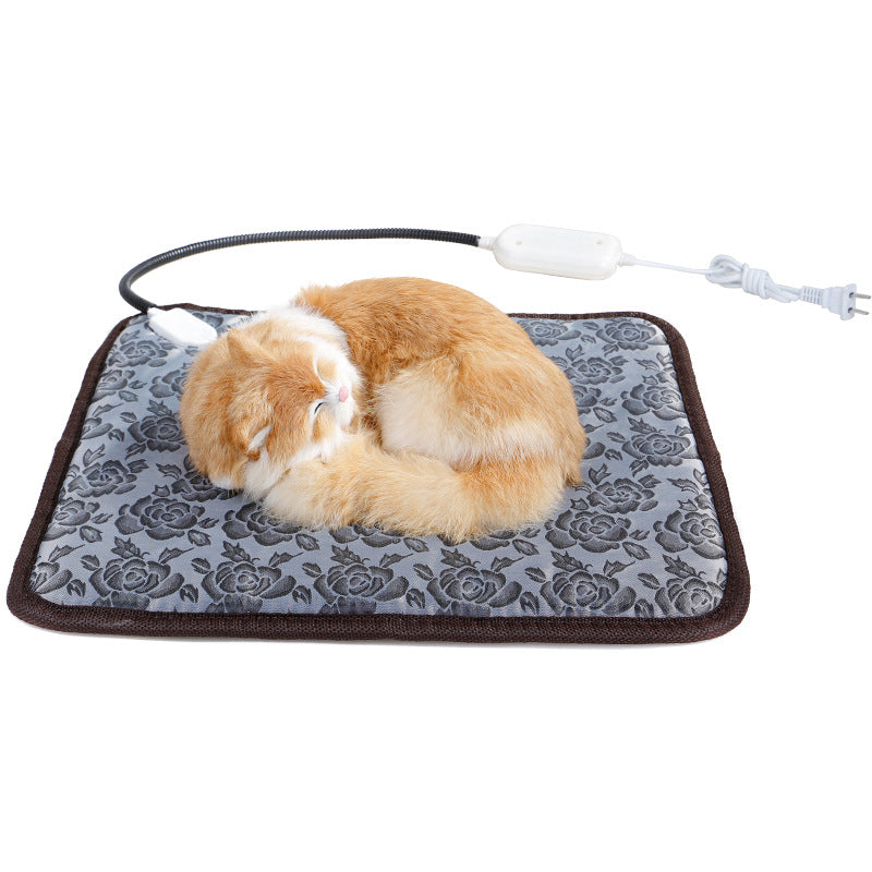 A plush orange cat sleeps on a gray rose-patterned electric pet heating pad with a chew-resistant power cord.