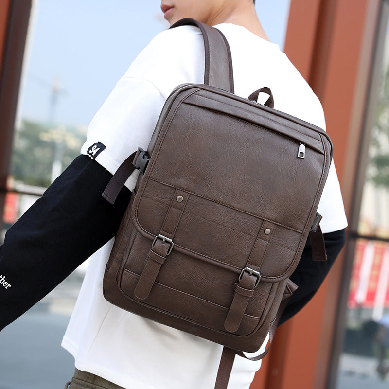 A person wearing a brown, retro-style faux leather backpack with double buckled straps and a zippered front pocket.
