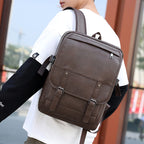 A person wearing a brown, retro-style faux leather backpack with double buckled straps and a zippered front pocket.