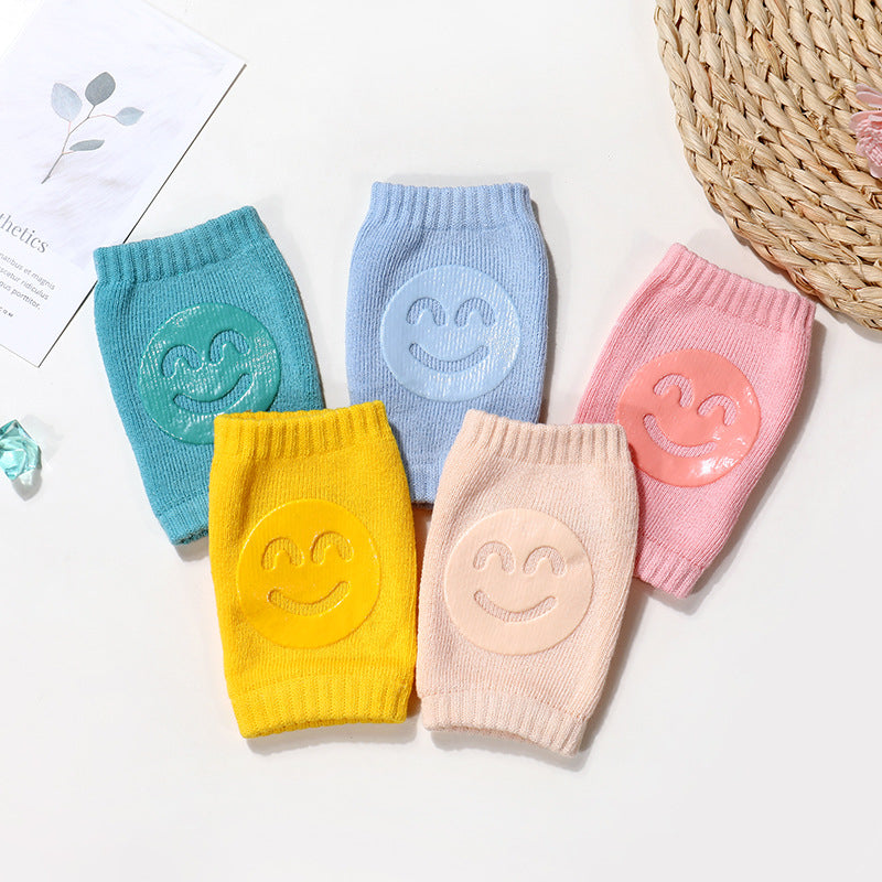 Five colorful, soft terry baby knee pads with silicone smiley face grips in teal, blue, yellow, peach, and pink.