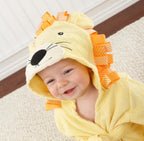 Baby wearing a soft, yellow cotton hooded lion bathrobe with orange ribbon mane accents on a white rug background.