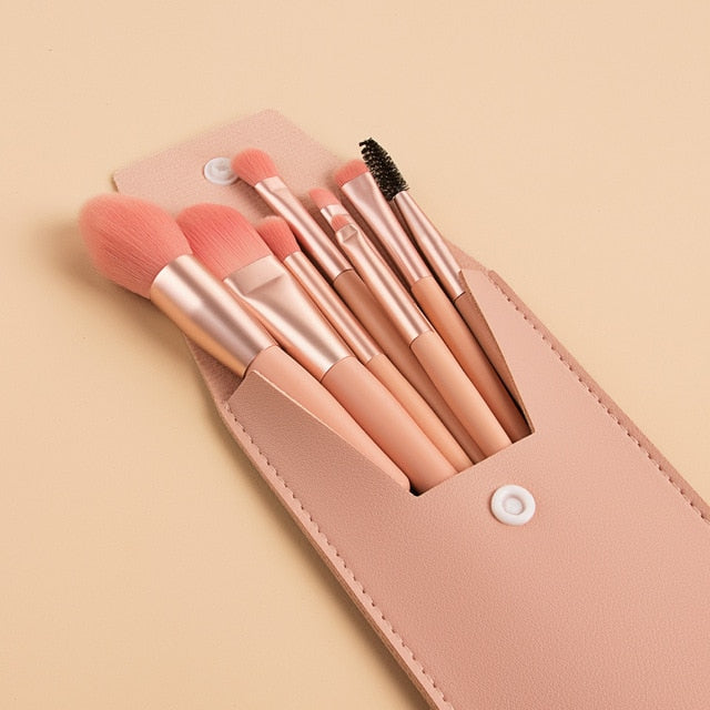 Eight mini makeup brushes with soft pink bristles and rose-gold handles in a matching portable faux leather pouch.