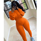 A woman wears an orange ribbed, long-sleeve crop top and matching high-waisted leggings leisure set.