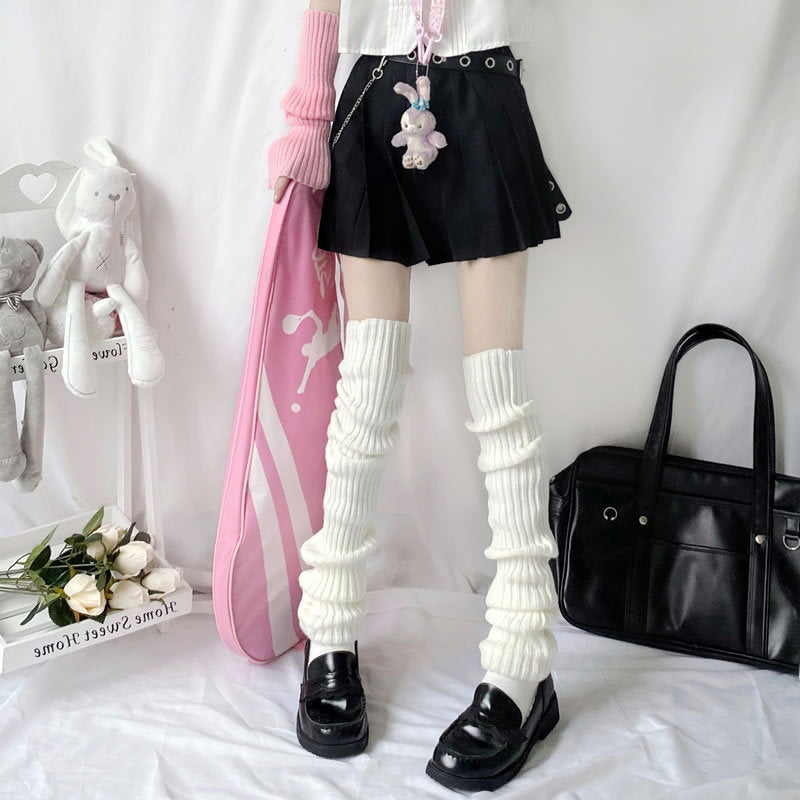 Person wearing white, rib-knitted slouchy leg warmers over white socks and black loafers with a black pleated skirt.