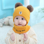 Baby wearing a yellow knit hat with two pom-poms and a matching scarf with "love me more" embroidery.