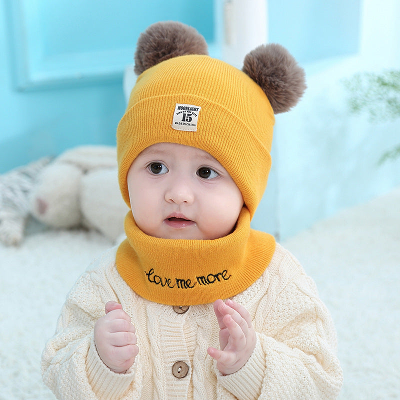 Baby wearing a yellow knit hat with two pom-poms, a "Moonlight 15" patch, and a matching "love me more" neck warmer.