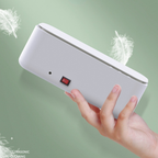 A white, handheld ultrasonic cleaner with a red power switch, displayed against a light green background with feathers.