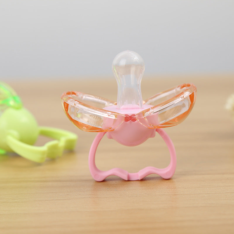 Pink and clear self-closing baby pacifier with a round silicone nipple and protective wings on a wooden surface.