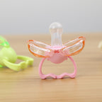 Pink and clear self-closing baby pacifier with a round silicone nipple and protective wings on a wooden surface.
