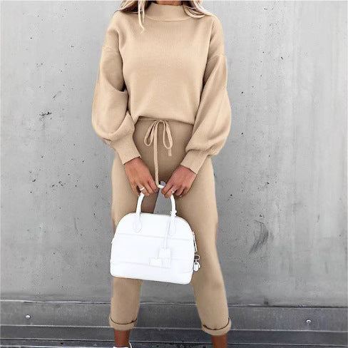 Beige two-piece fleece sweater set with high neck, long balloon sleeves, and drawstring pants holding a white handbag.