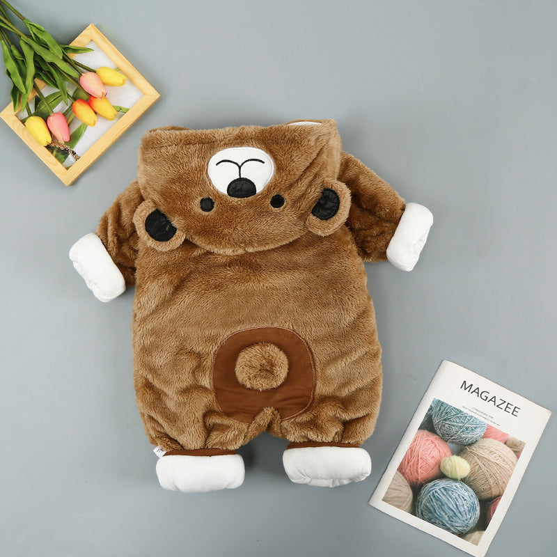 Brown plush bear onesie with a hooded face, white cuffs, and belly patch on a gray background with flowers and a book.