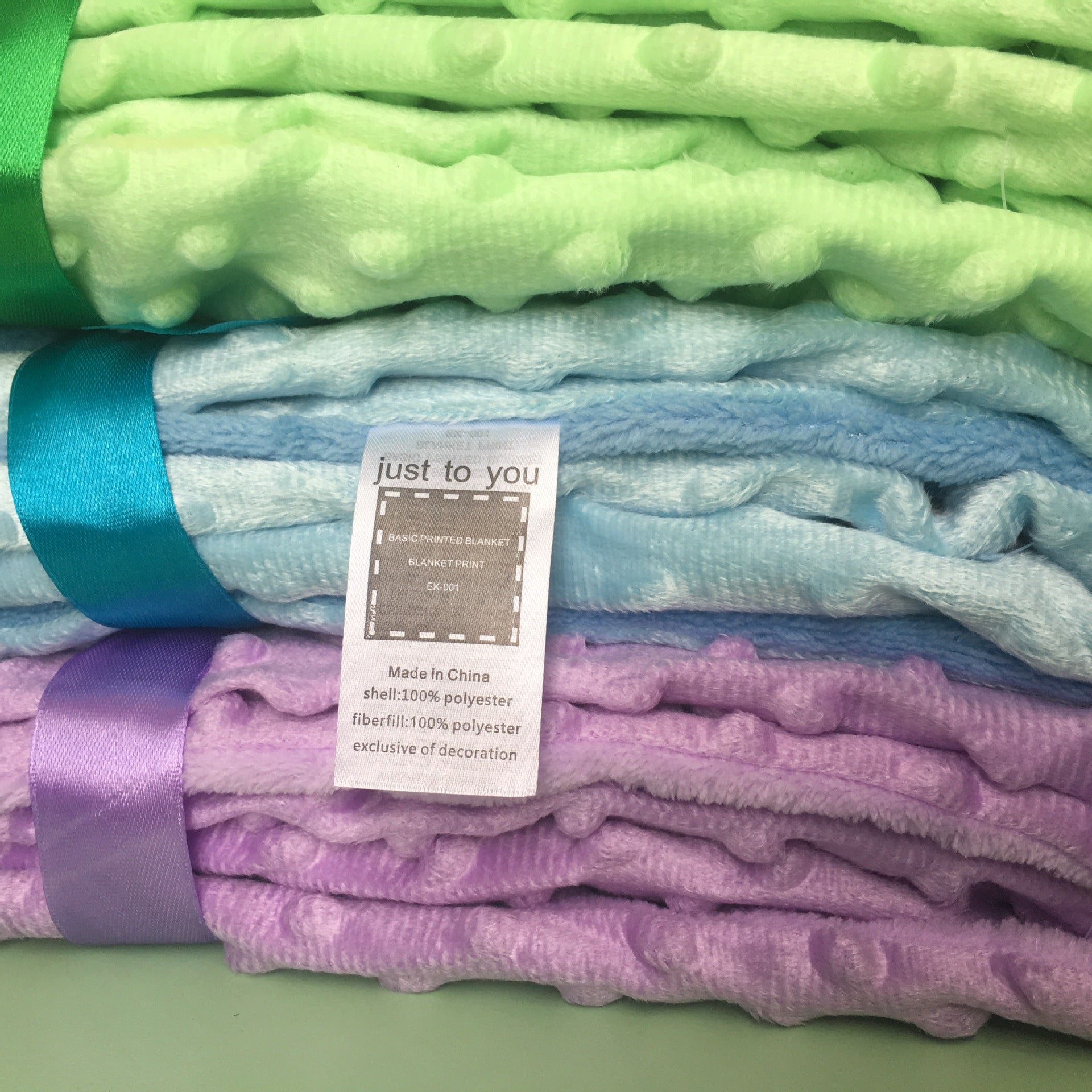 Stacked lime green, baby blue, and lavender soft dimple-dot polyester baby blankets tied with matching satin ribbons.
