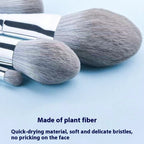 Set of soft, grey plant-fiber makeup brushes with silver ferrules on a light blue background.