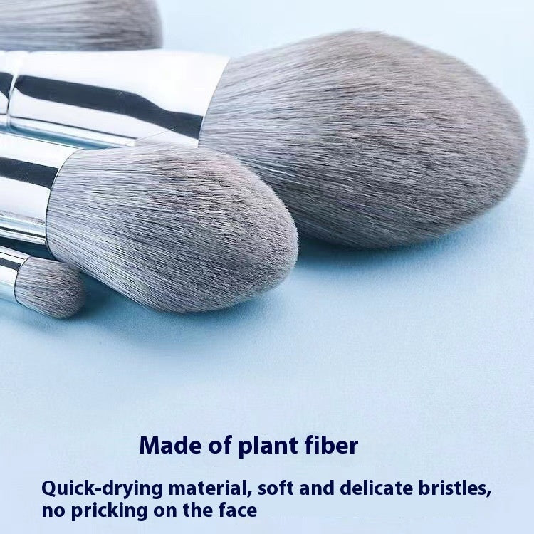 Set of soft, grey plant-fiber makeup brushes with silver ferrules on a light blue background.
