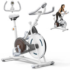 White stationary exercise bike with a brown flywheel, digital console, and a woman riding in the background.