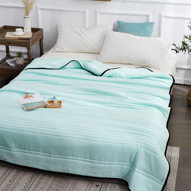 Mint green, quilted summer cooling blanket with black trim, draped over a bed in a modern, light-filled bedroom.