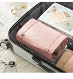 A pink, rectangular, 4-in-1 folding travel organizer bag with metal fasteners, packed inside an open suitcase.