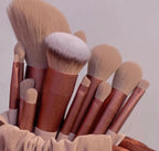 A 13-piece set of makeup brushes with metallic rose gold handles and soft tan synthetic bristles in a fabric pouch.
