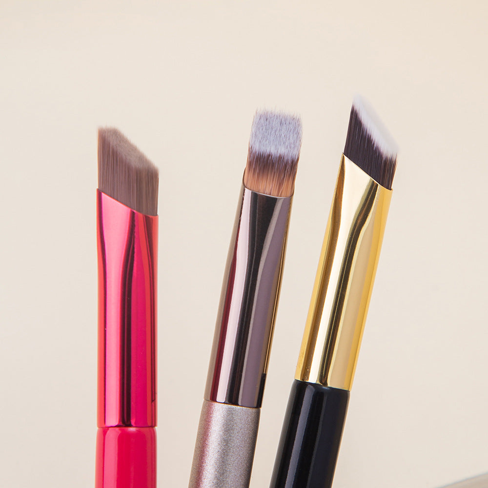 Three makeup brushes with angled and flat synthetic bristles, featuring vibrant red, metallic, and gold handles.