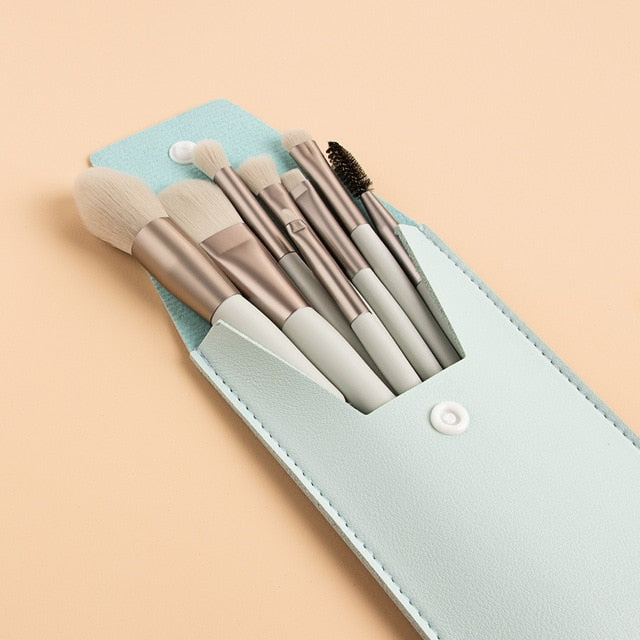 Mini makeup brush set in a light blue snap-close leather pouch with soft, taupe-handled brushes on a peach background.