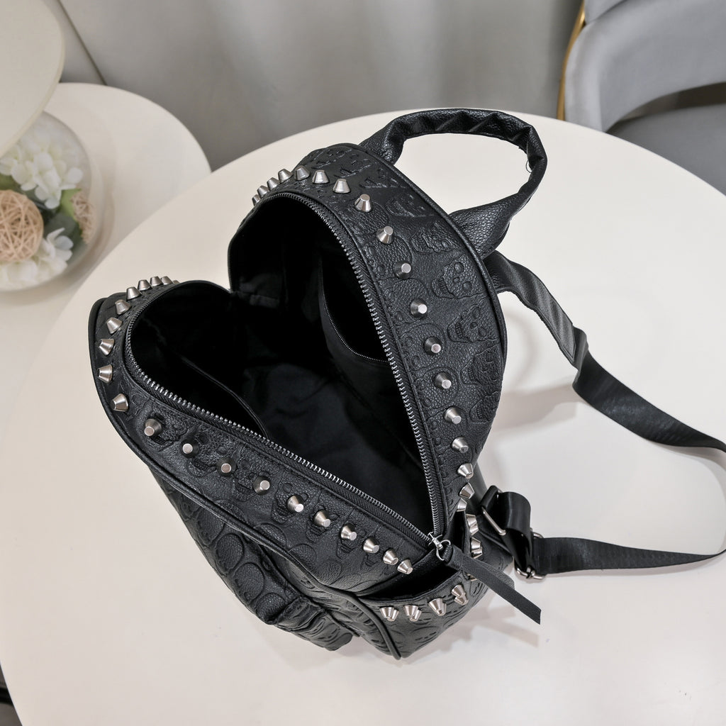 Black soft leather backpack with skull embossing, silver rivet studs, top handle, and adjustable shoulder straps.