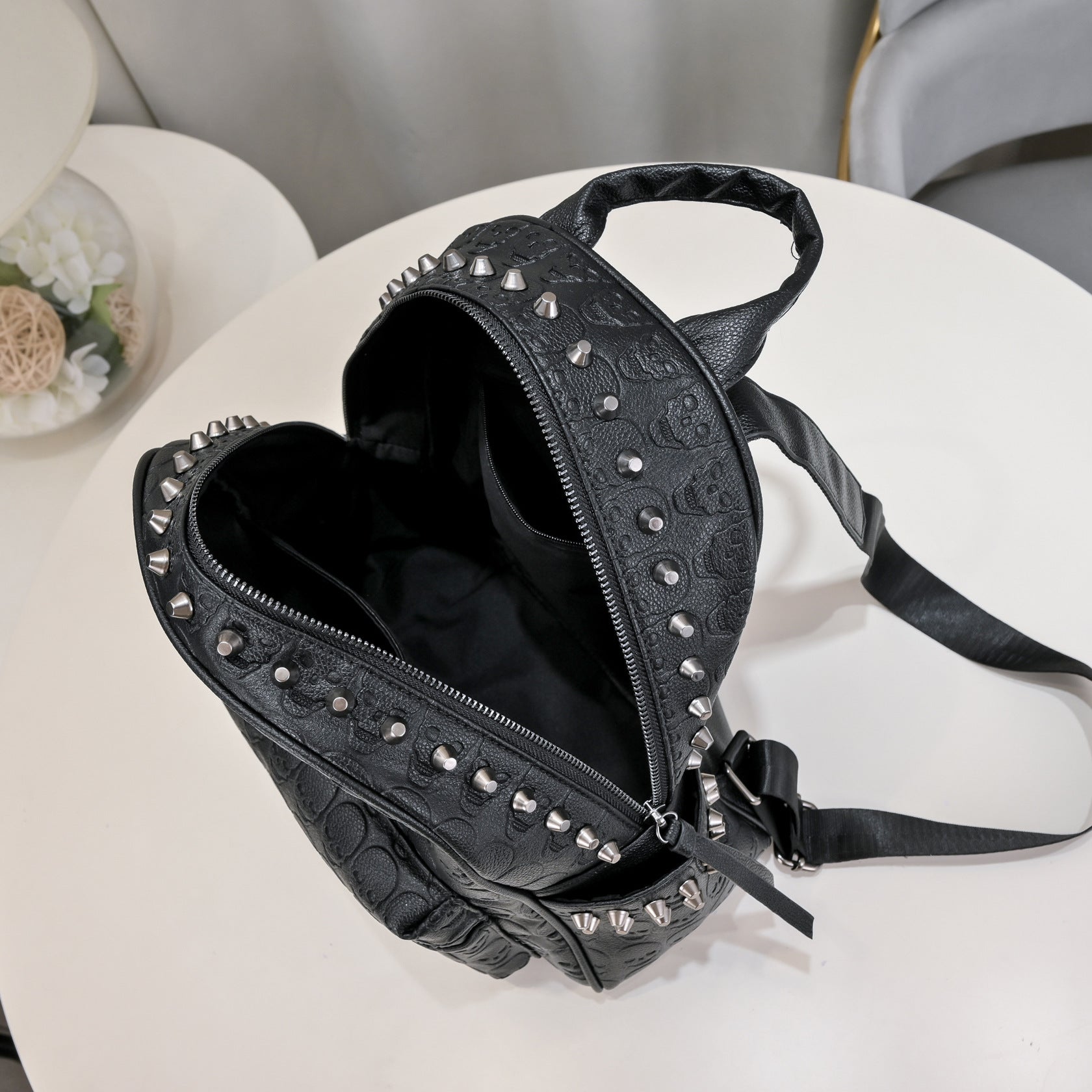 Black soft leather backpack with skull embossing, silver rivet studs, top handle, and adjustable shoulder straps.