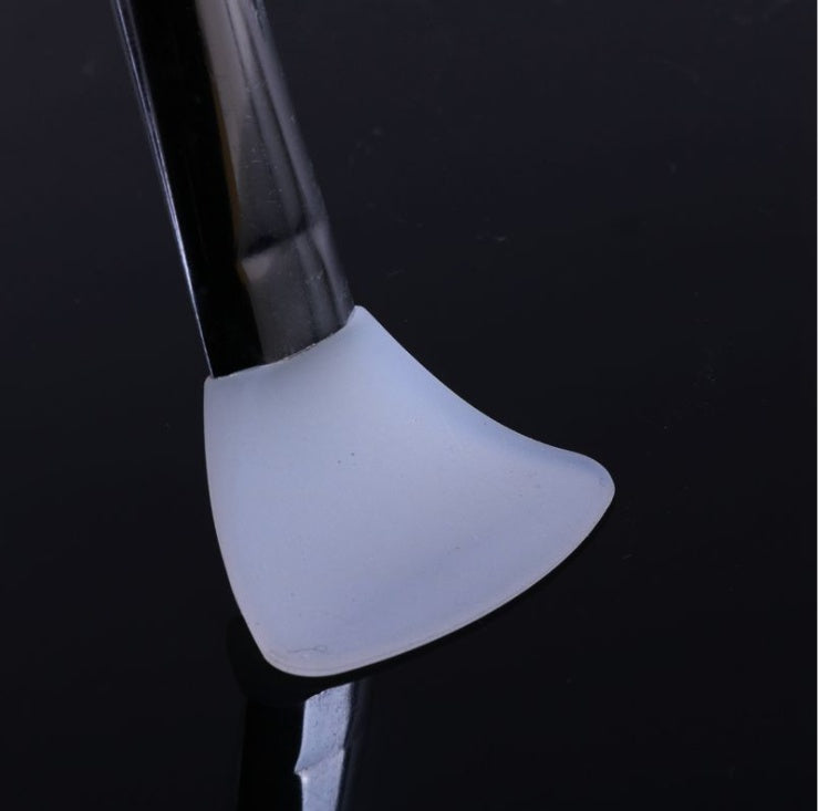 A close-up of a white silicone mask applicator brush with a black handle against a dark, reflective background.