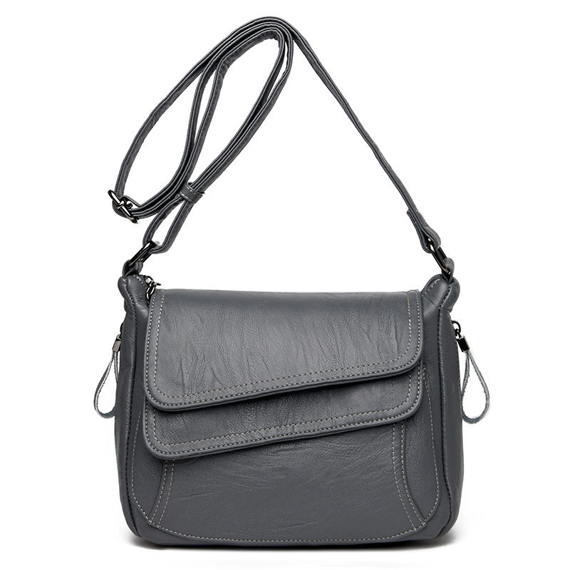Grey soft leather crossbody bag with an adjustable strap, top flap, and white contrast stitching.