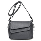 Grey soft leather crossbody bag with an adjustable strap, top flap, and white contrast stitching.