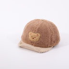 Brown fuzzy baby cap with a beige corduroy brim and a cute bear patch, isolated on a white background.