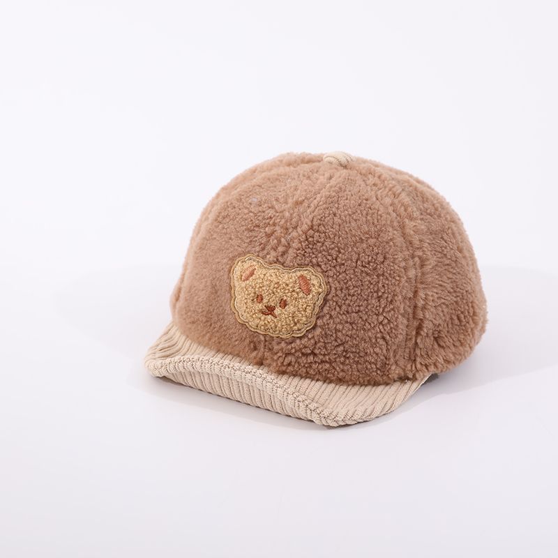 Brown fuzzy baby cap with a beige corduroy brim and a cute bear patch, isolated on a white background.
