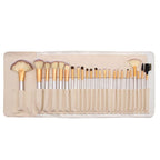 Set of 24 champagne-handled synthetic makeup brushes with creamy white bristles, arranged in a matching leatherette roll.