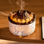 Volcano-shaped humidifier with white and black crackle finish, emitting glowing orange light and mist on a wooden table.