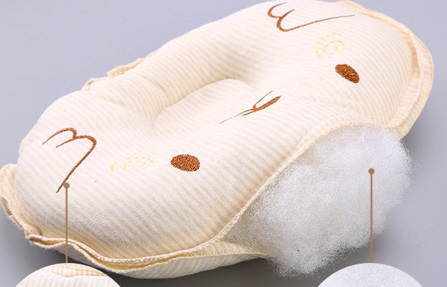 Cream-colored, striped, baby head-support pillow with embroidered face details and visible soft polyester stuffing.