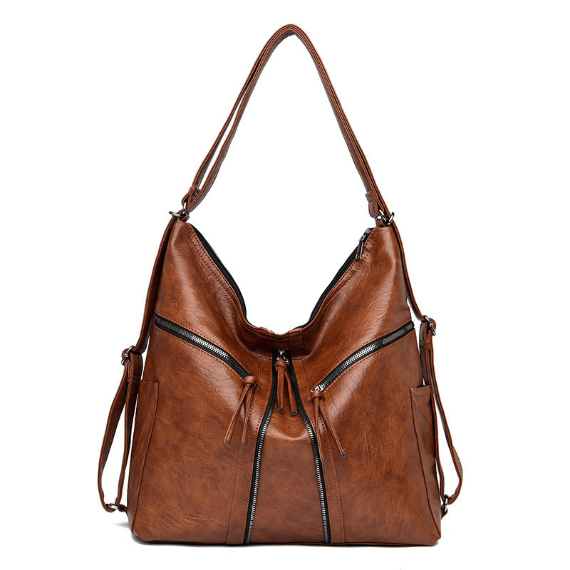 Brown soft leather convertible shoulder bag and backpack with decorative front zippers and tassels, isolated on white.