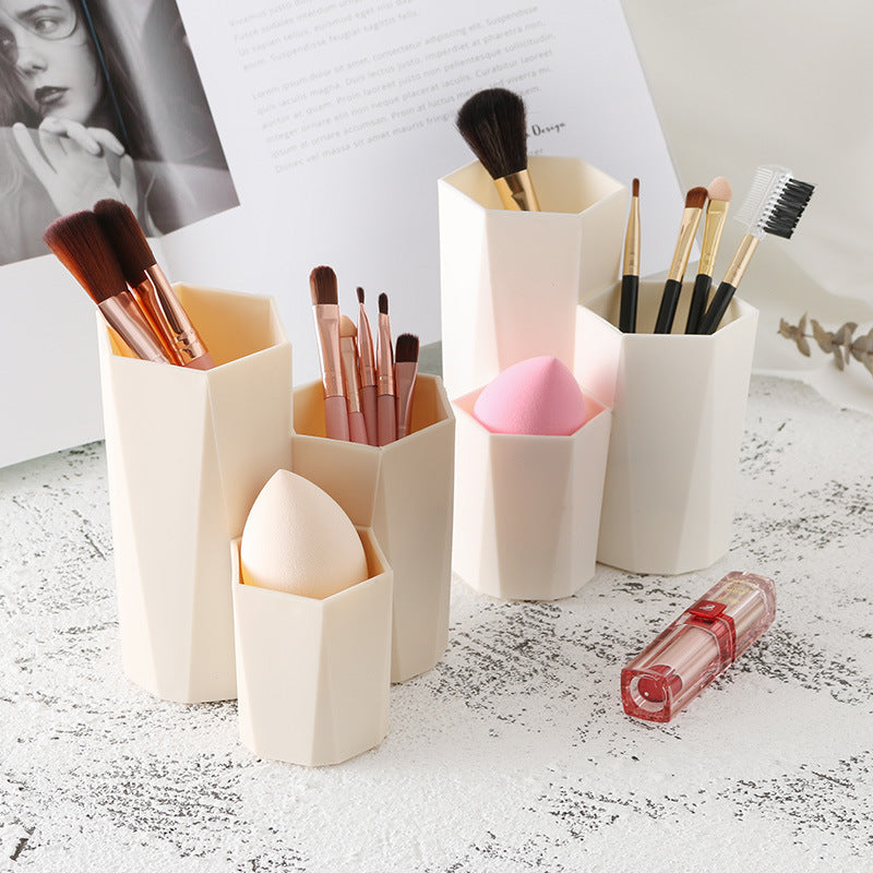 Beige, geometric plastic makeup brush holders of varying heights, containing brushes and beauty sponges.
