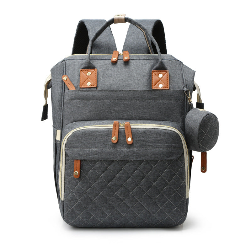 Grey quilted mummy backpack with tan leather accents, top handles, multiple compartments, and a matching side pouch.